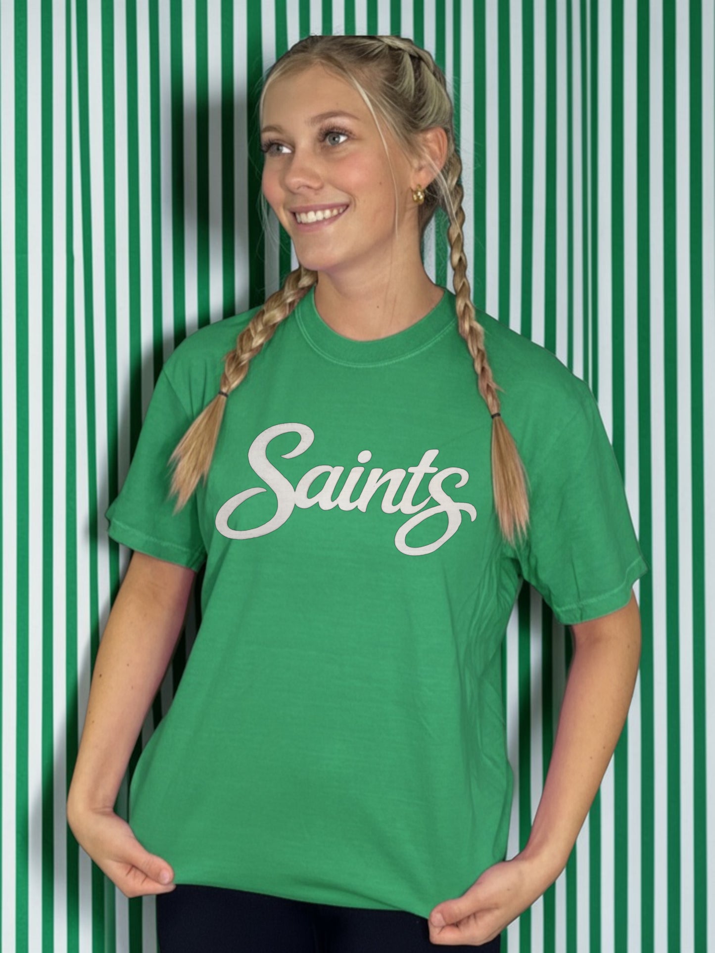 Person wearing a green 'Saints' t-shirt against a green and white striped background