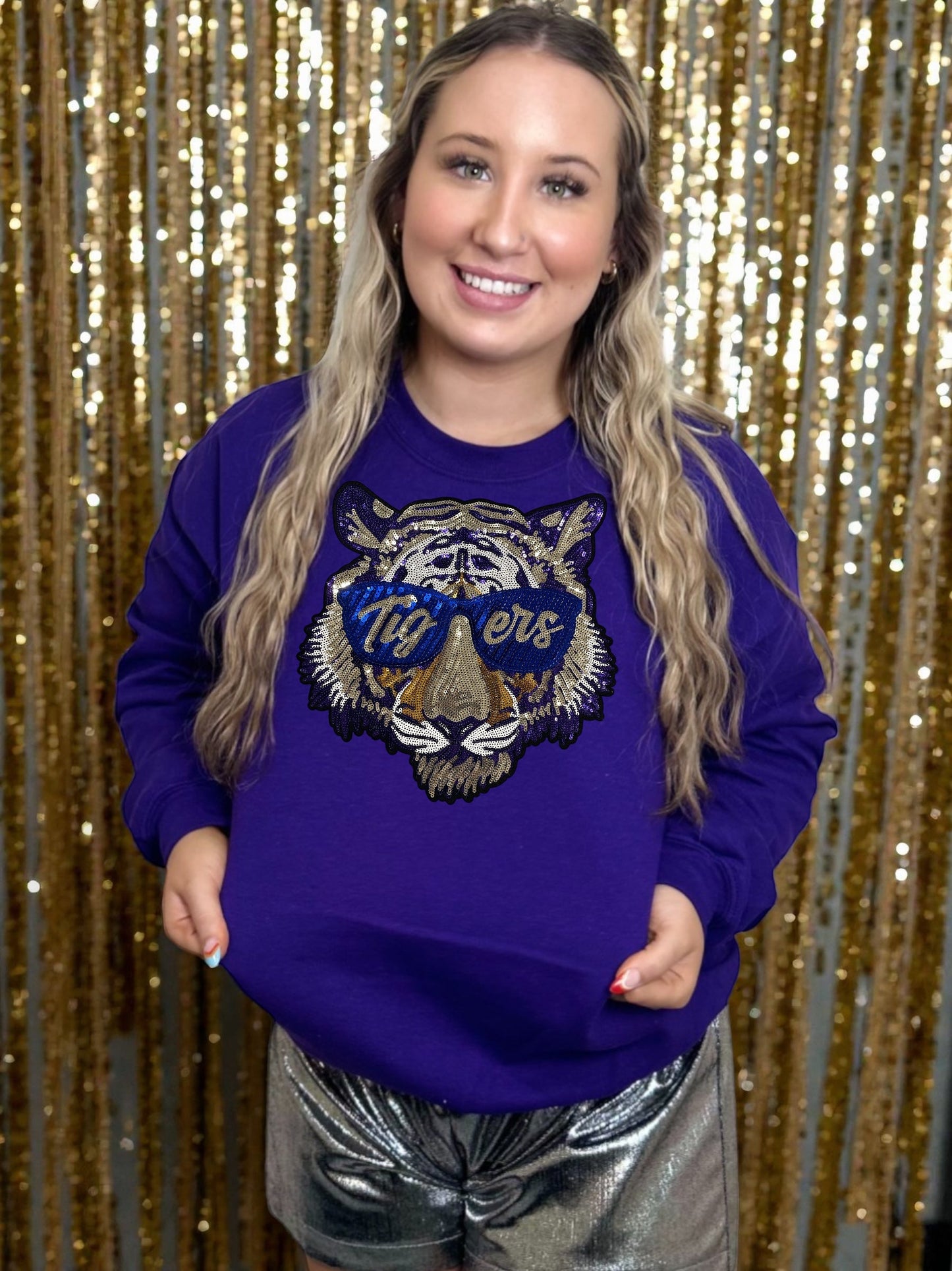 Person wearing a purple sweatshirt with a tiger logo in front of a glittery gold and silver background