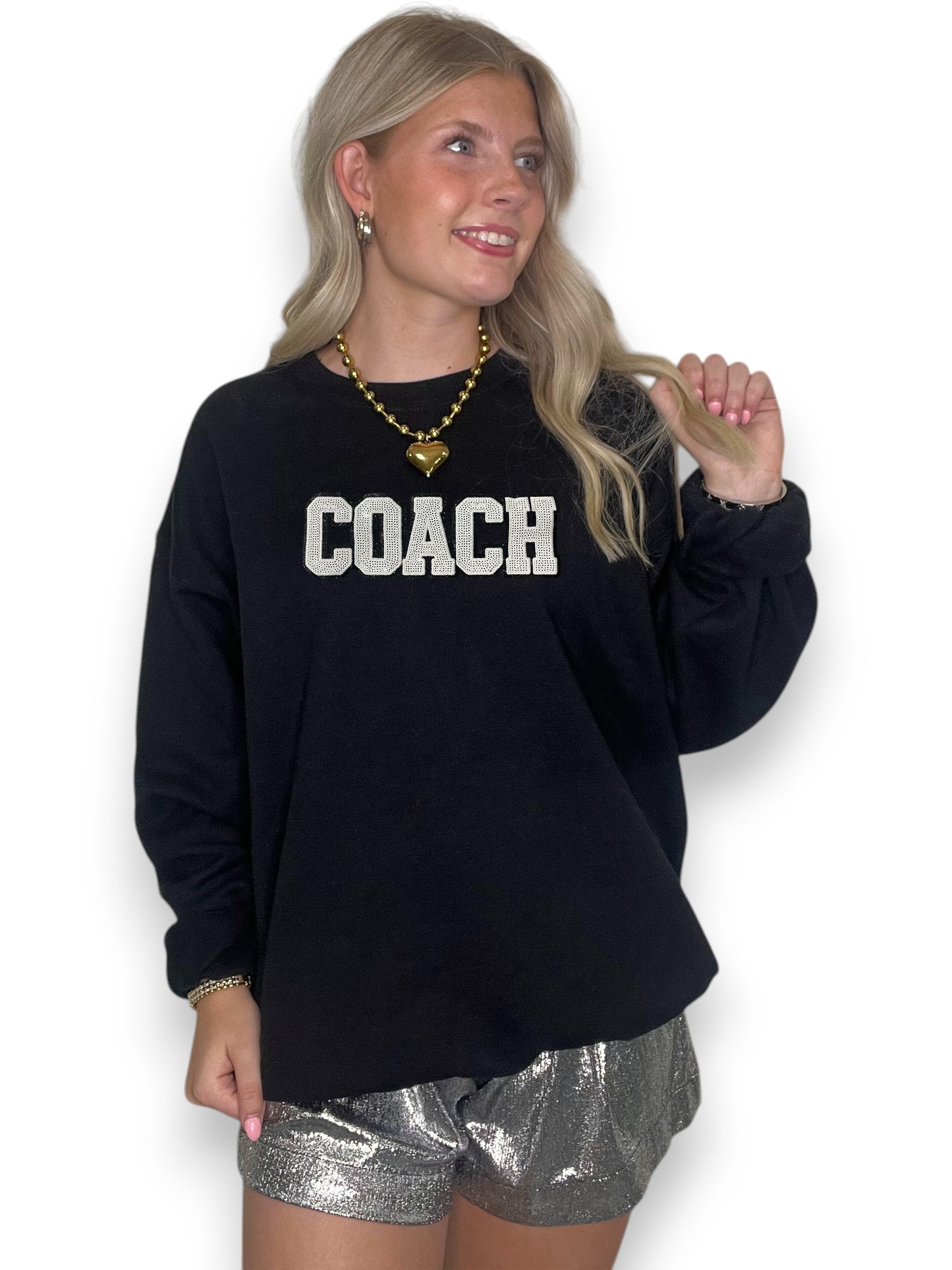 Woman wearing a black sweatshirt with 'COACH' text and silver shorts on a white background