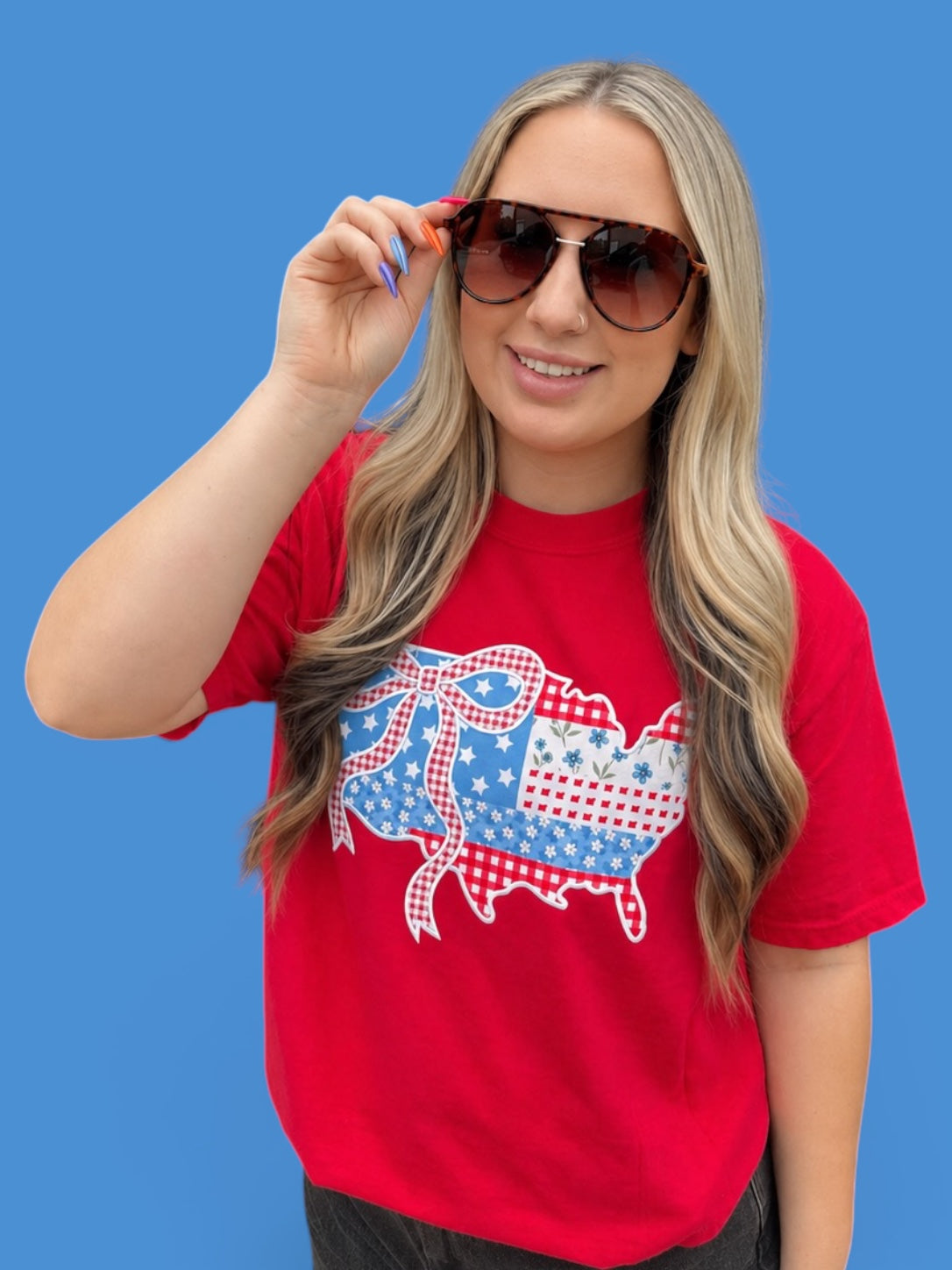Woman wearing a red t-shirt with a graphic design, holding sunglasses against a blue background