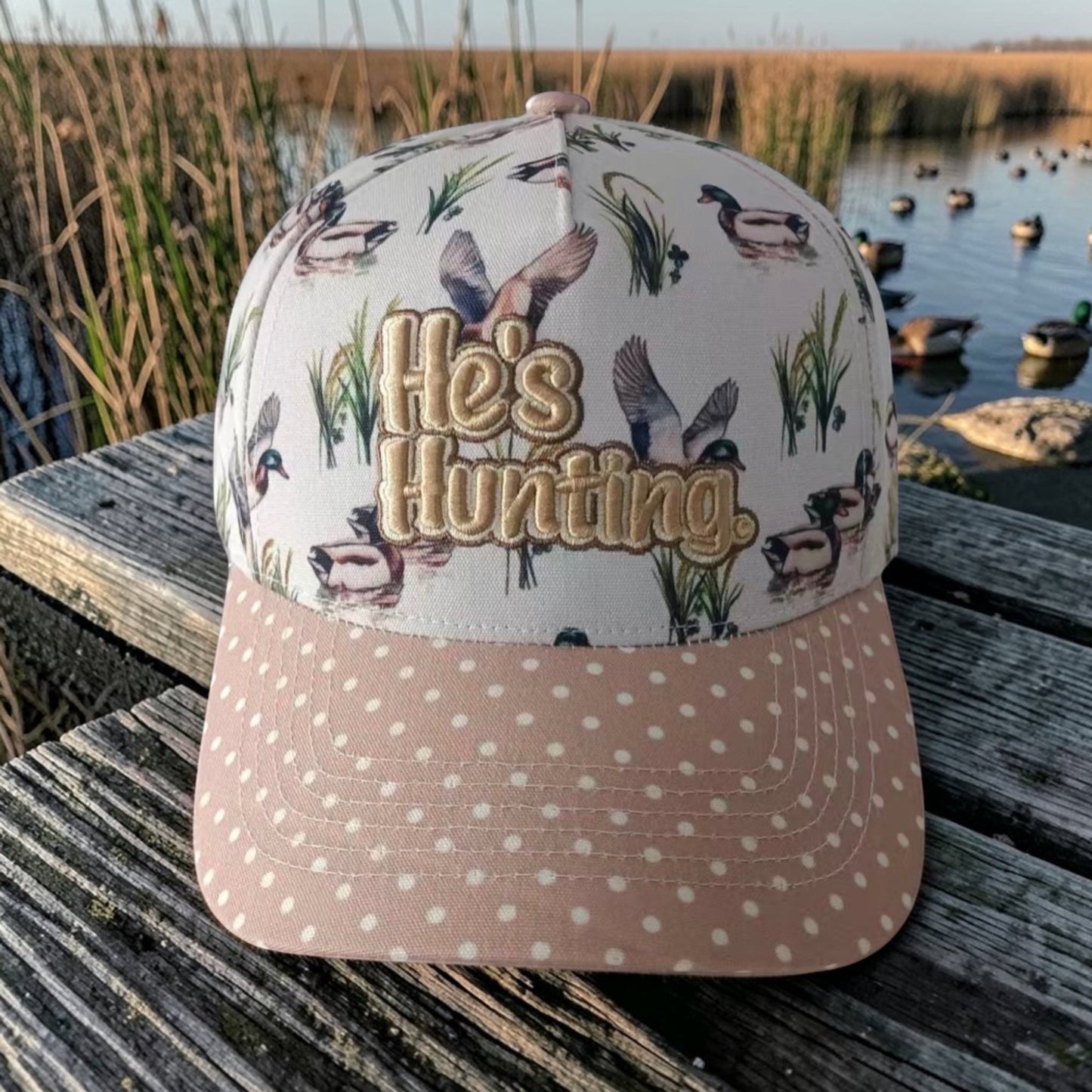 6J Wholesale He's Hunting cap with duck print fabric and pink polka dot brim. Features embroidered text and snapback closure.