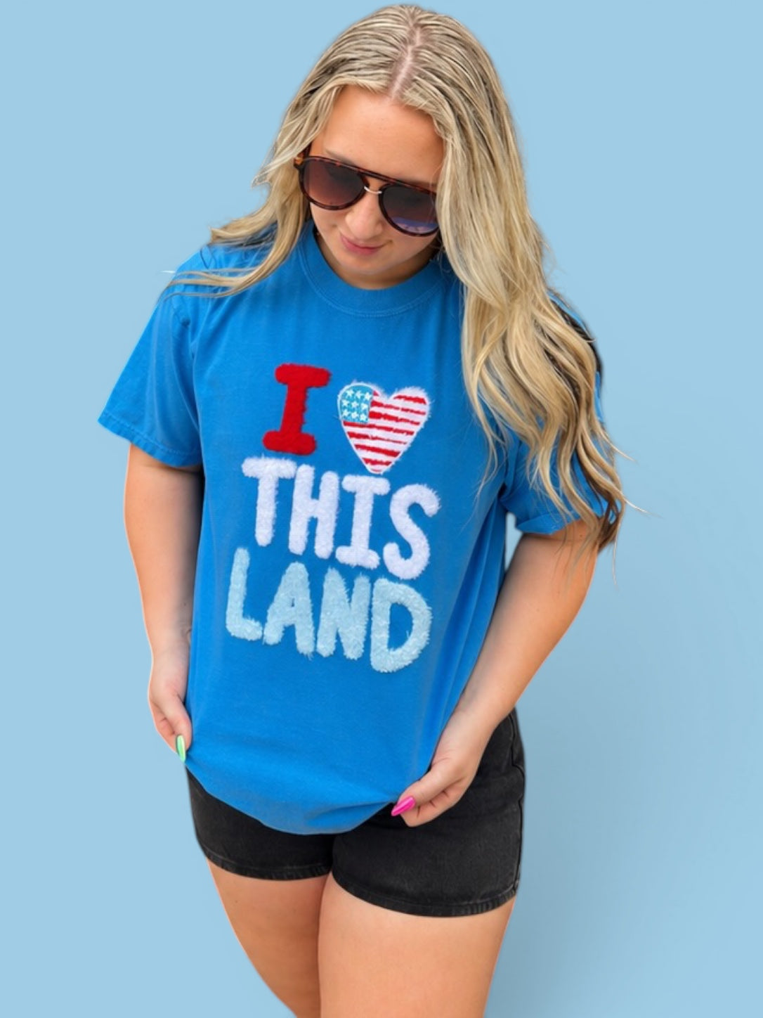 Woman wearing a blue t-shirt with 'I love this land' text against a light blue background