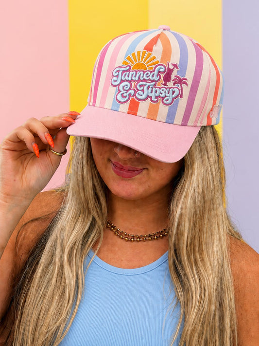 Person wearing a colorful striped cap with 'Tanned & Tippy' logo against a multicolored background