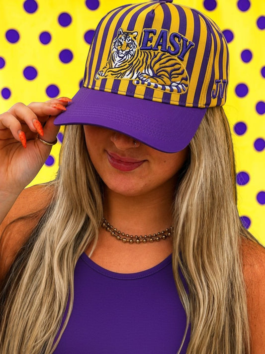 Person wearing a purple and yellow striped cap with a tiger logo and 'EASY' text on a polka dot background.