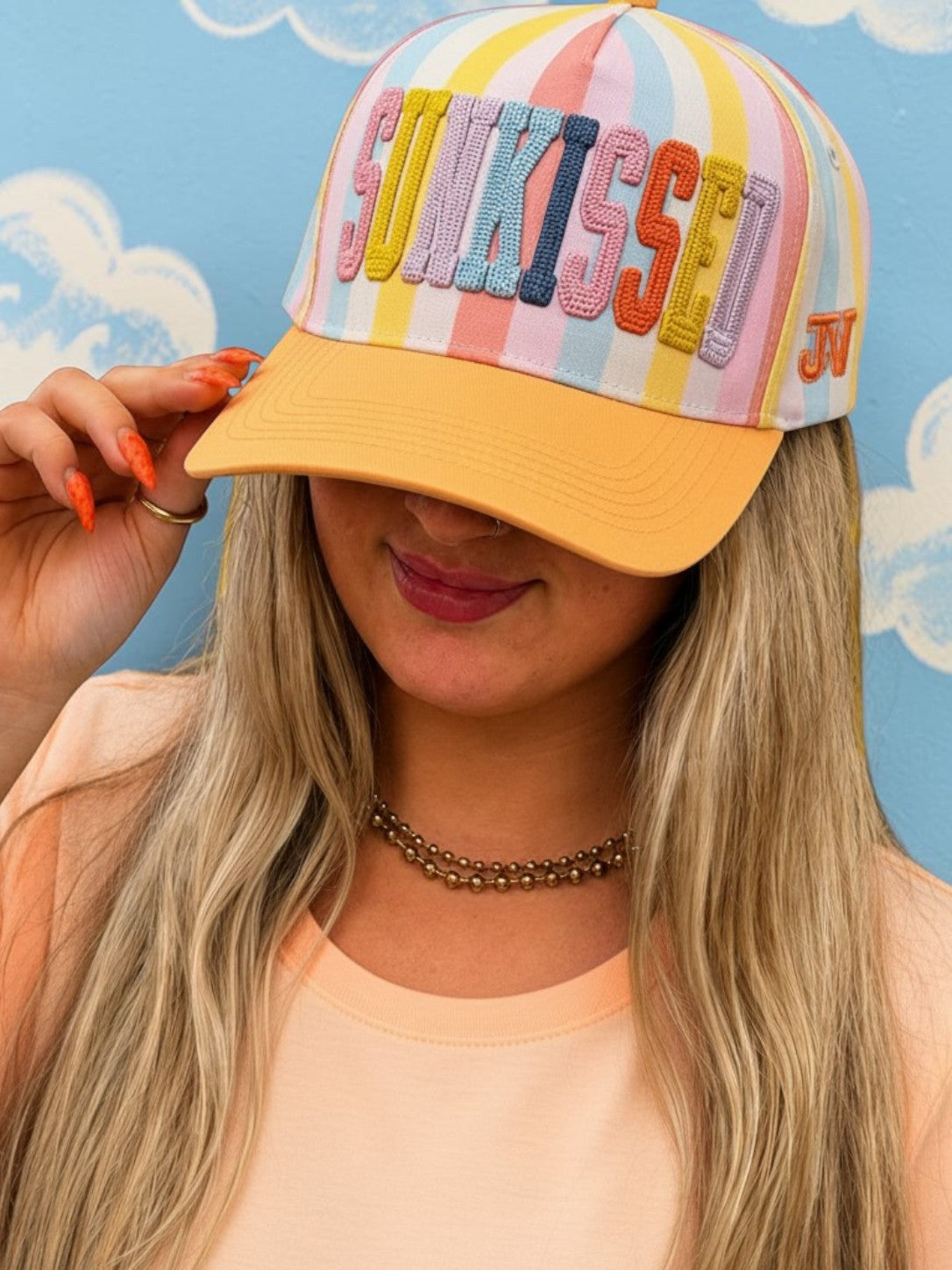 Person wearing a colorful striped cap with 'Sunkissed' text against a blue background