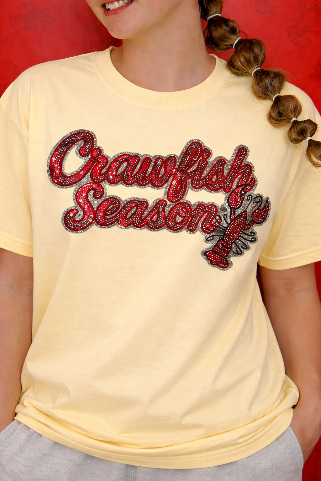 Child wearing a yellow t-shirt with 'Crawfish Season' text and crawfish graphic against a red background