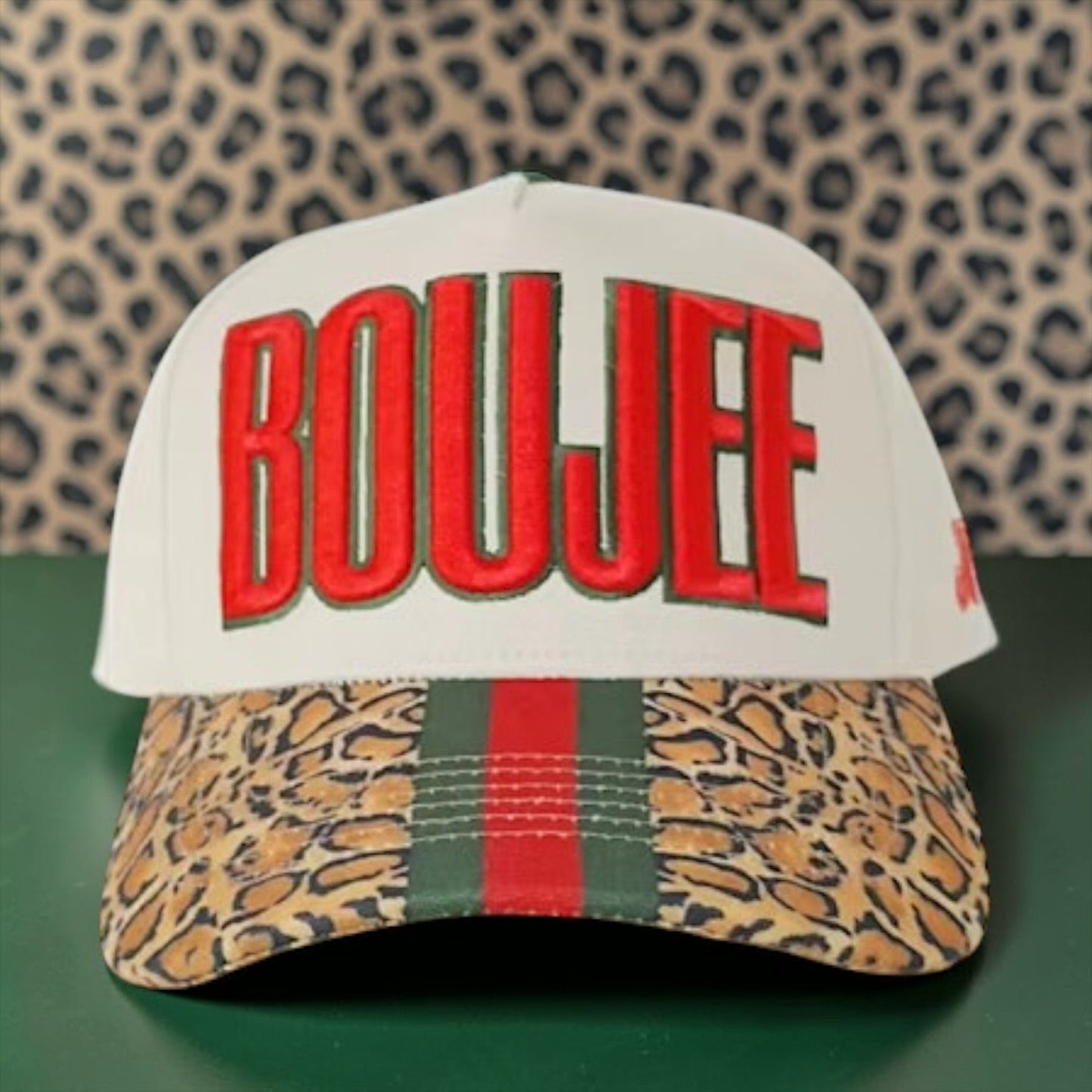Cap with 'BOUJEE' text and leopard print design on a green surface with cheetah pattern background