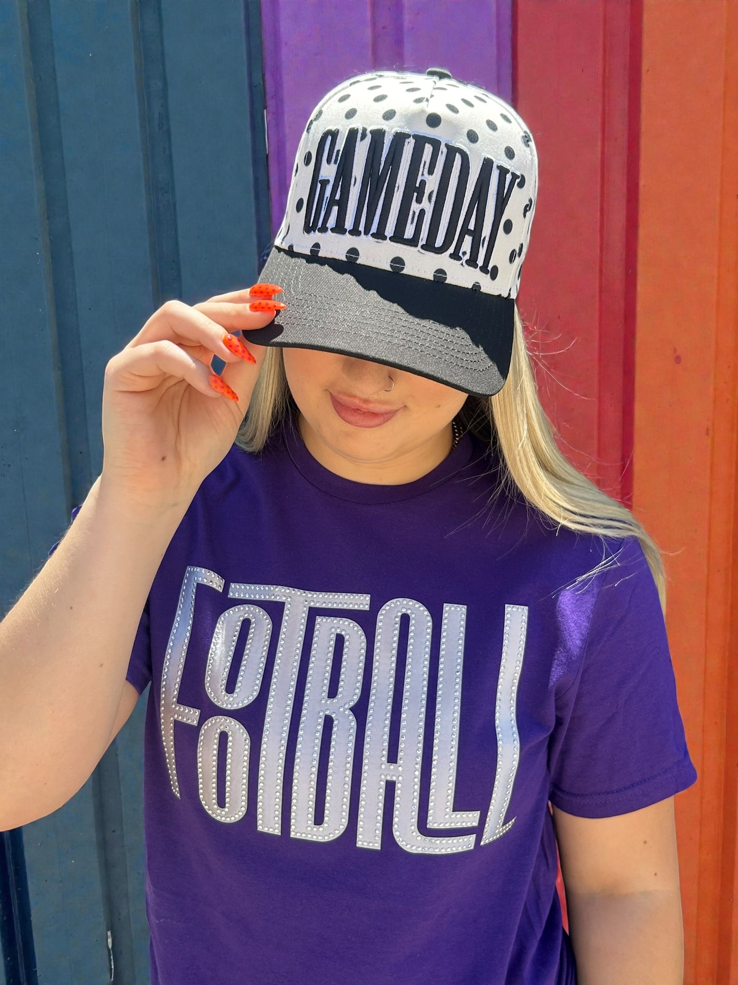 Person wearing a purple 'FOOTBALL' t-shirt and a cap with 'GAMEDAY' text against a colorful background.