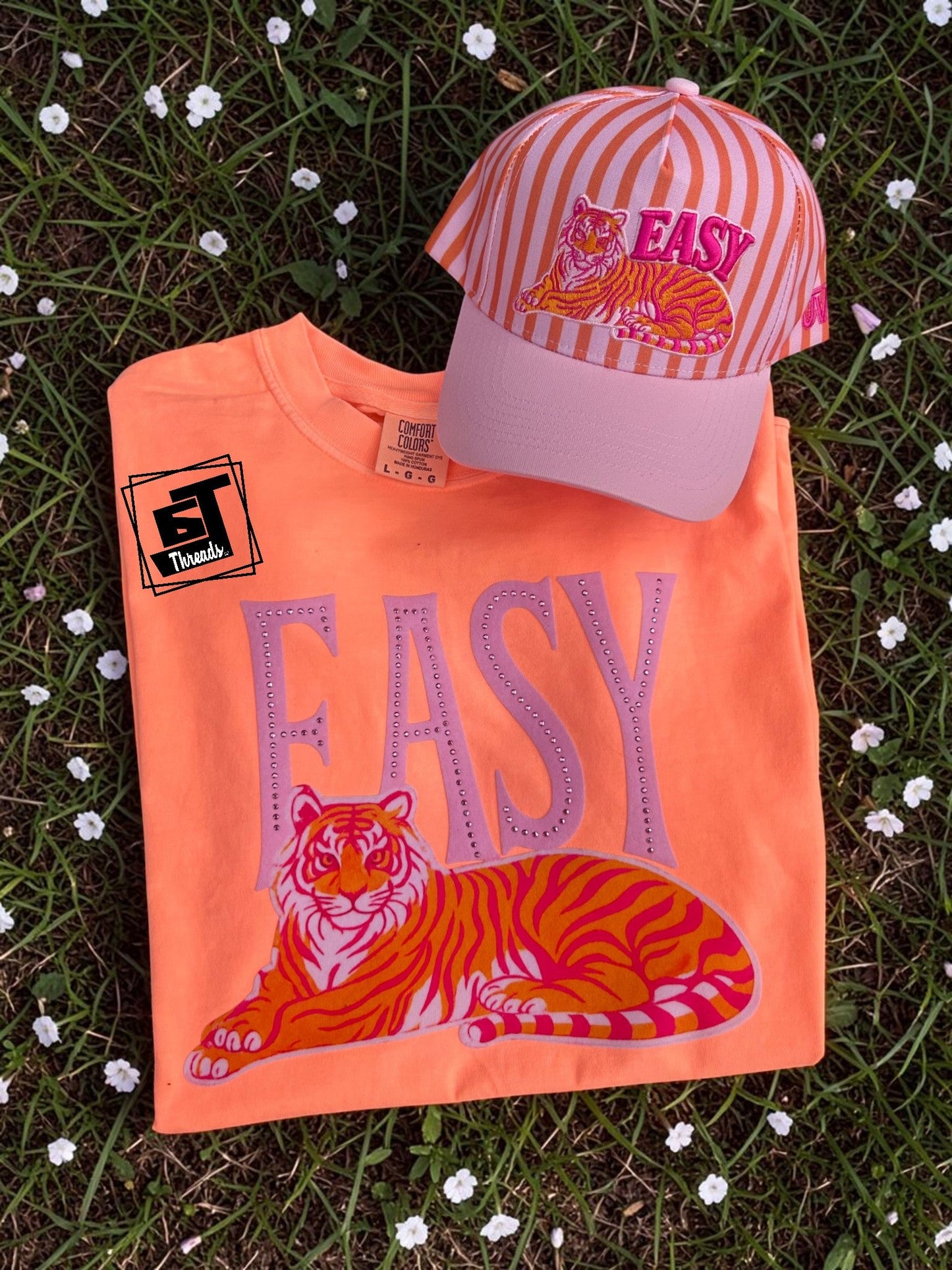 Orange t-shirt with tiger design and 'EASY' text, paired with a matching cap on grass.