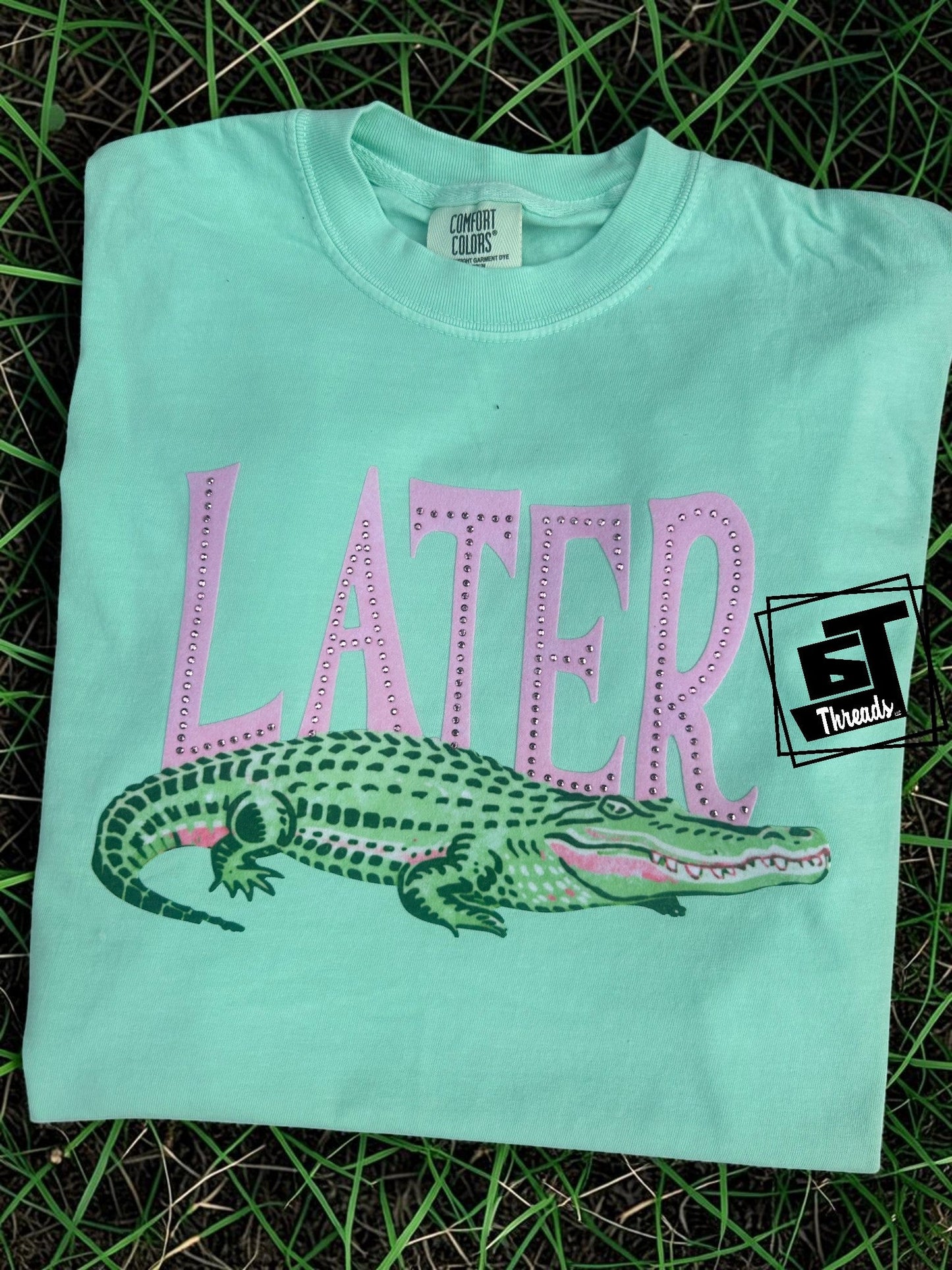 Light blue t-shirt with pink 'LATER' text and alligator graphic on grass