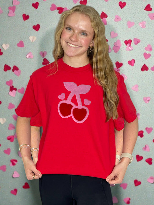 Person wearing a red t-shirt with a heart and bow design against a heart-patterned background