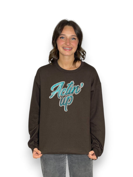 Person wearing a brown sweatshirt with 'Actin' Up' text on a white background