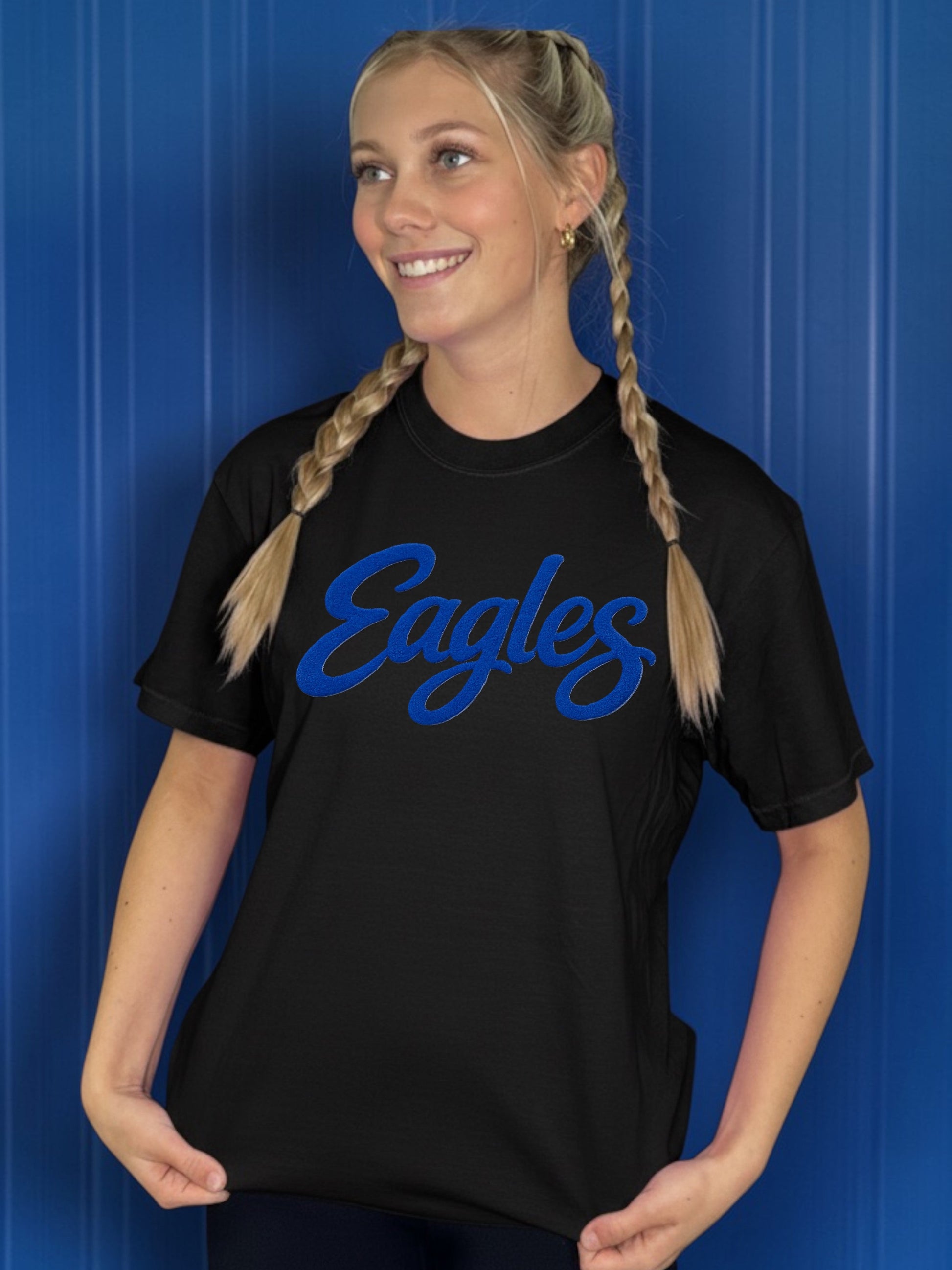 Person wearing a black t-shirt with 'Eagles' printed in blue against a blue background