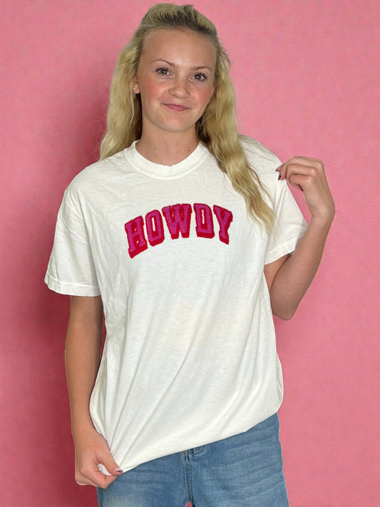 Person wearing a white t-shirt with 'HOWDY' in red text against a pink background