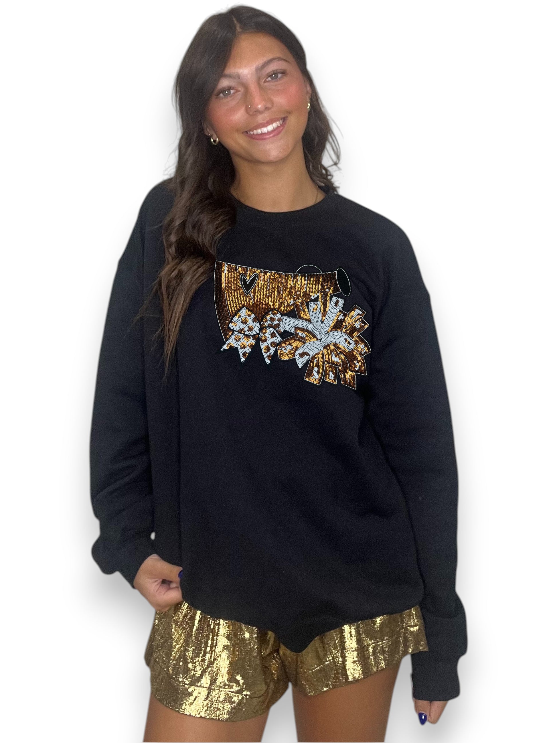 Woman wearing a black sweatshirt with a graphic design and gold sequin shorts on a white background