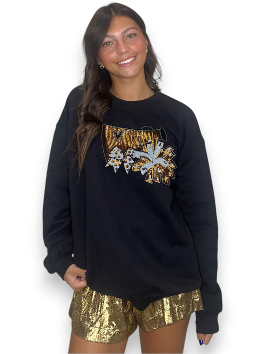 Woman wearing a black sweatshirt with a graphic design and gold sequin shorts on a white background