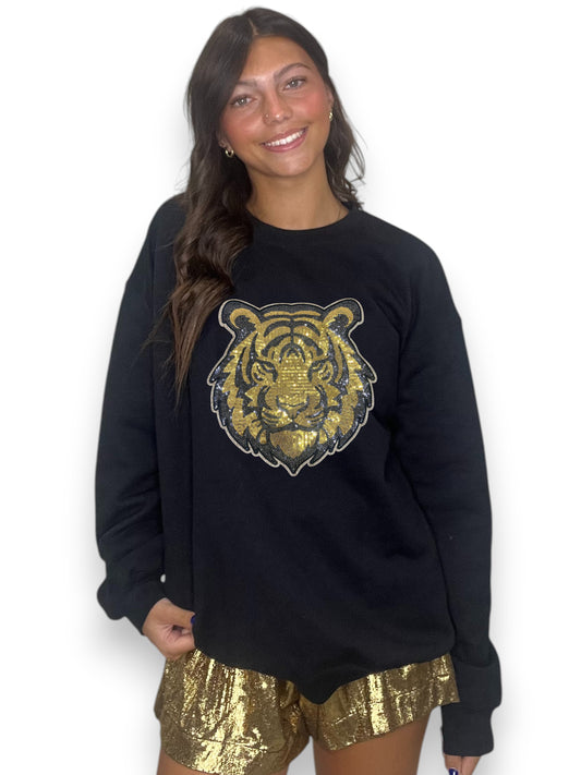 Woman wearing a black sweatshirt with a gold tiger design and gold shorts on a white background