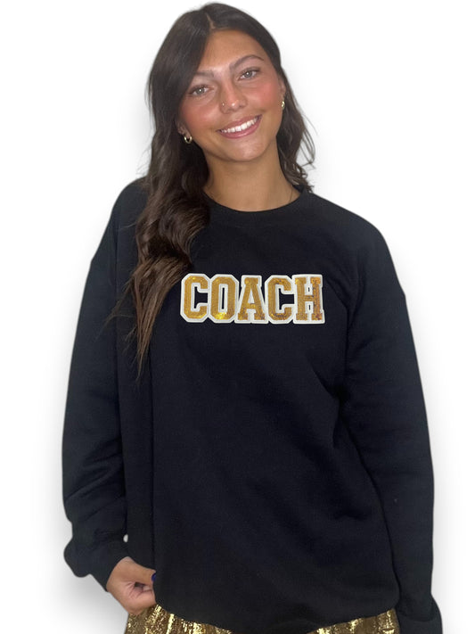 Woman wearing a black sweatshirt with 'COACH' in gold letters on a white background