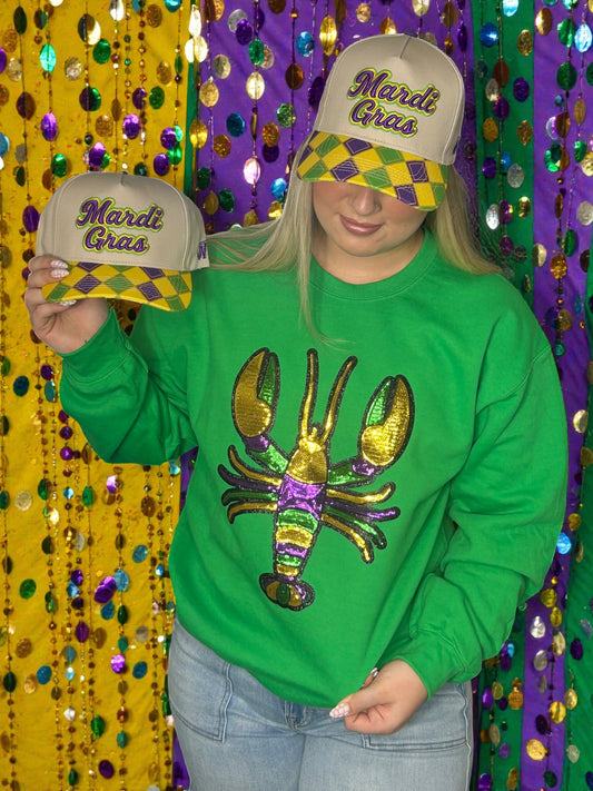 Person wearing a green sweatshirt with a colorful crawfish design and Mardi Gras hats against a festive background.