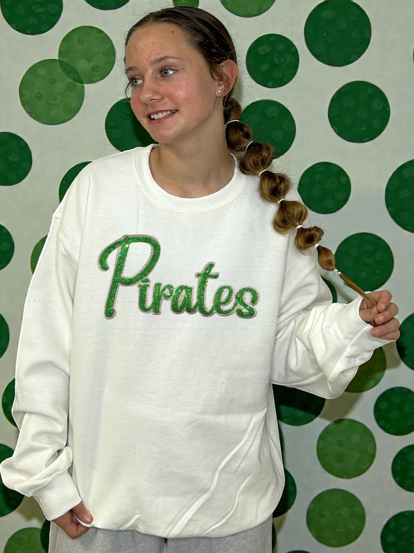 Person wearing a white sweatshirt with 'Pirates' on it against a green polka dot background