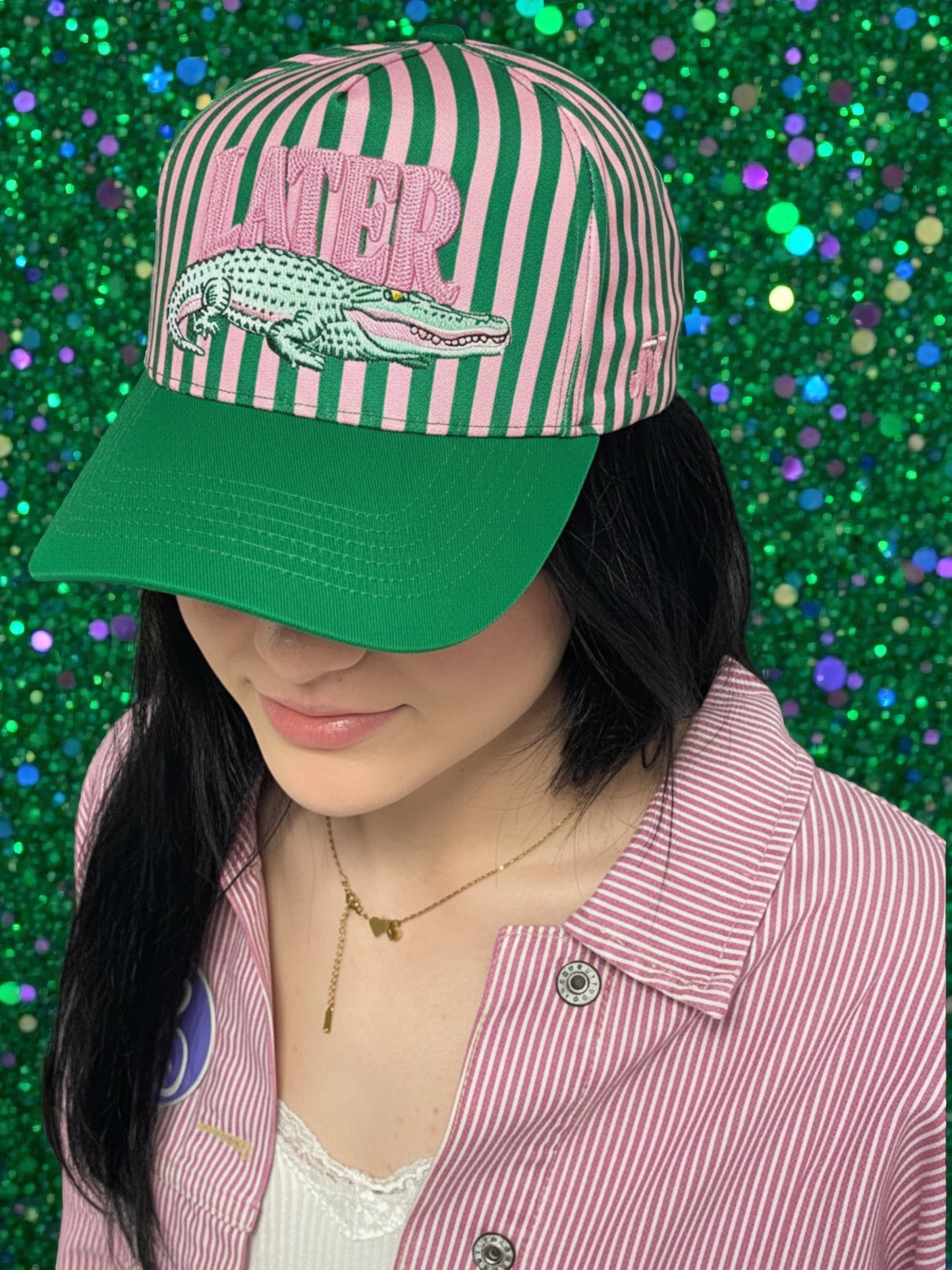 Person wearing a striped cap with an alligator graphic and 'LATER' text on a glittery green background.