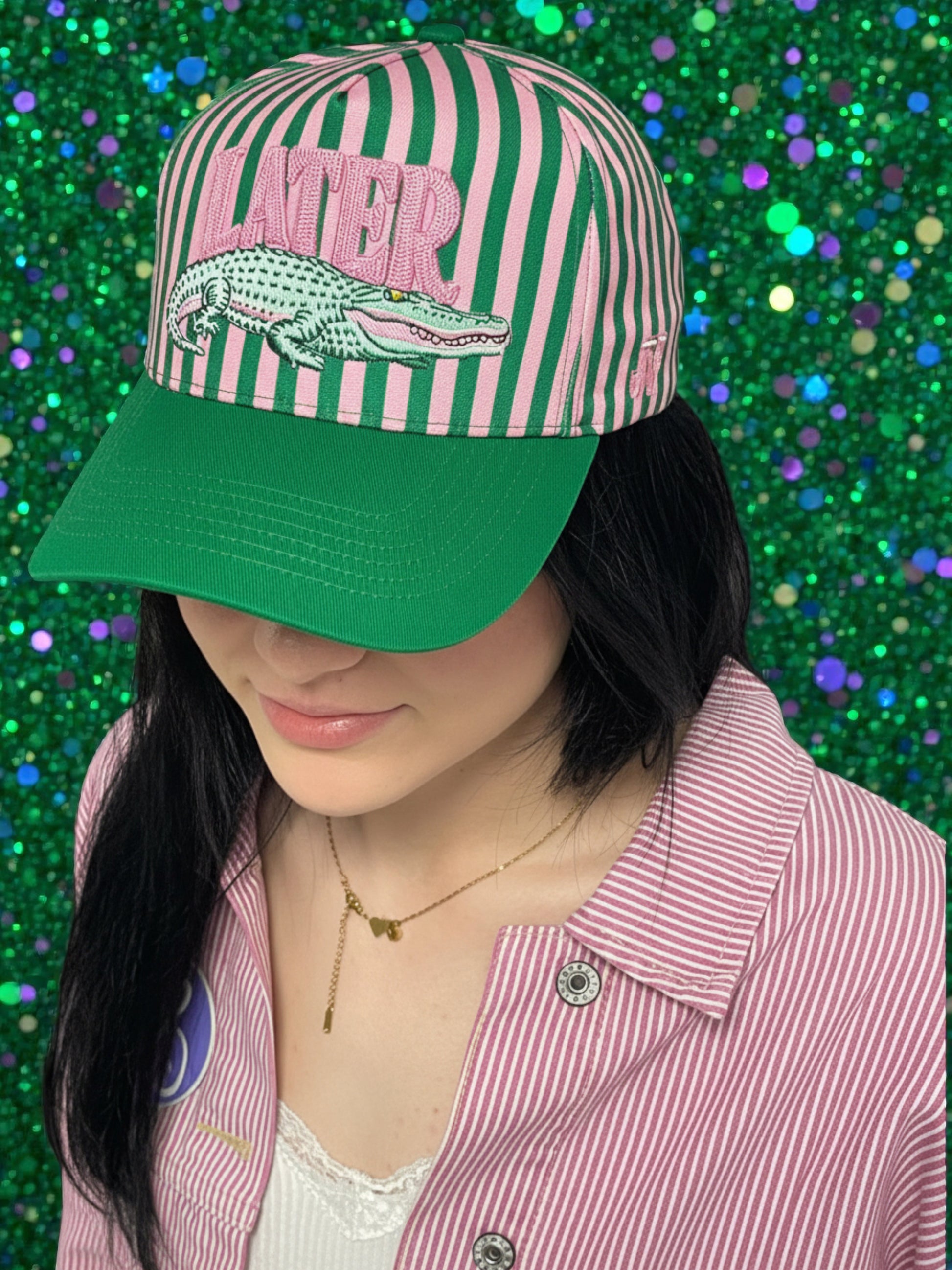 Person wearing a striped cap with an alligator graphic and 'LATER' text on a glittery green background.