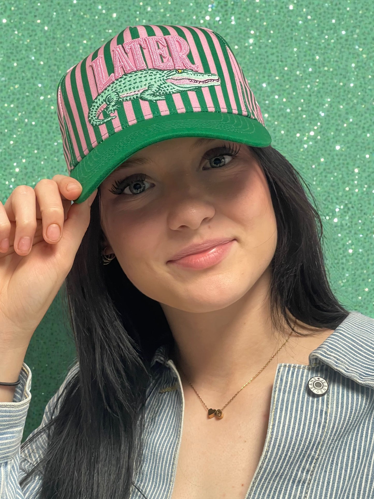 Person wearing a green and pink striped cap with a logo on a green gator background