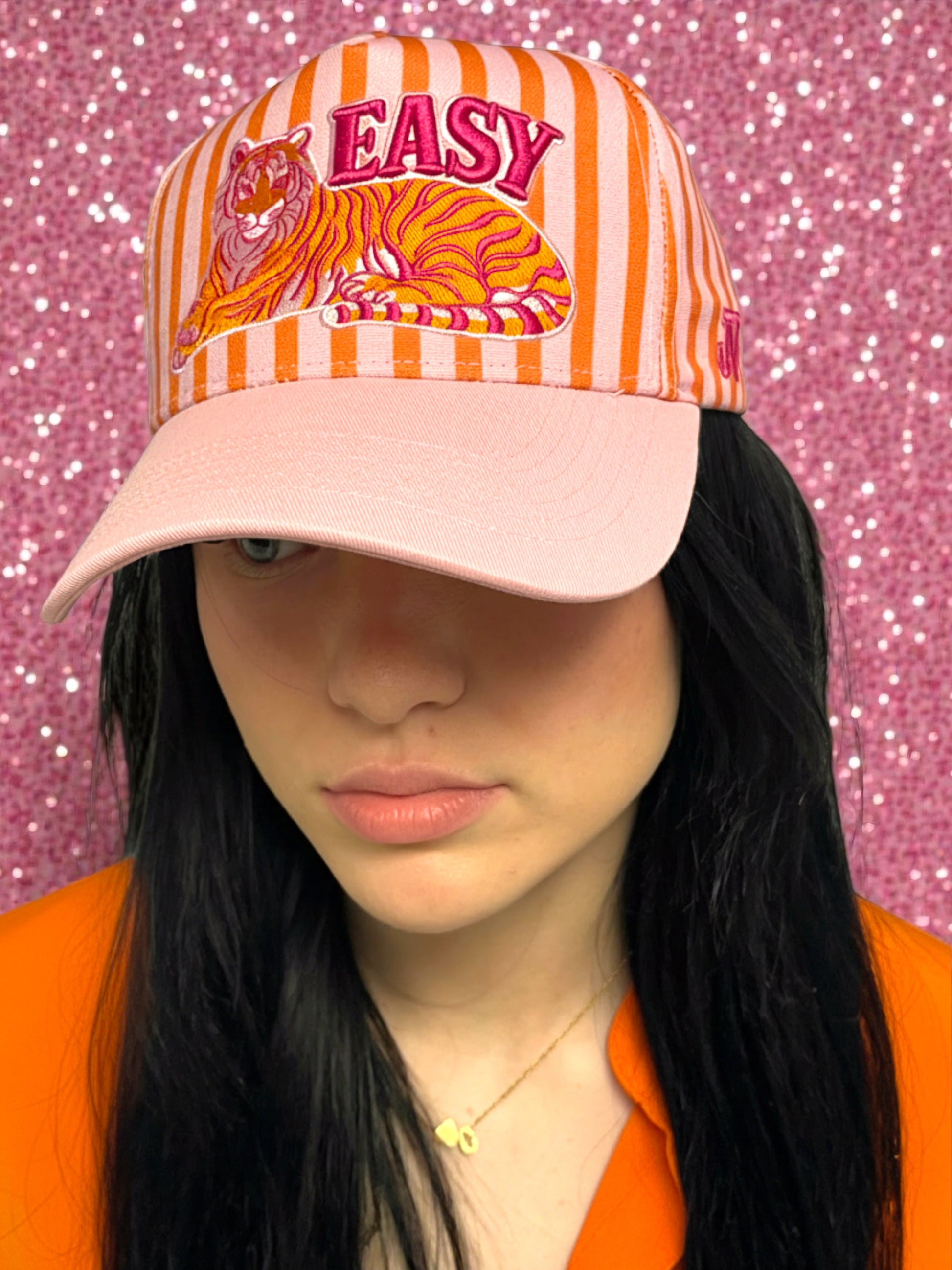 Person wearing a cap with a tiger design and 'EASY' text on a pink glittery background