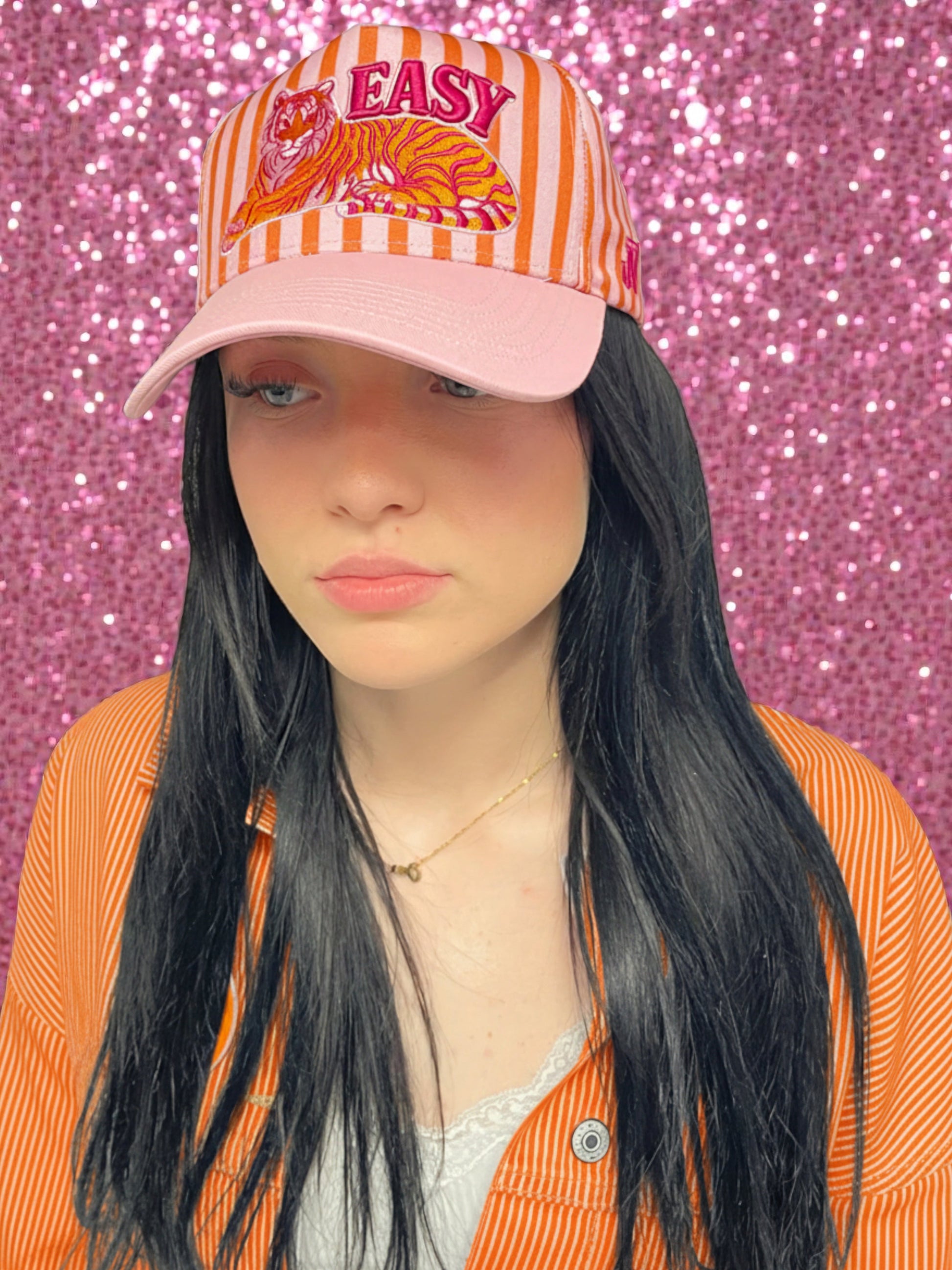 Person wearing a pink and orange striped cap with a tiger design and 'EASY' text against a pink glittery background.