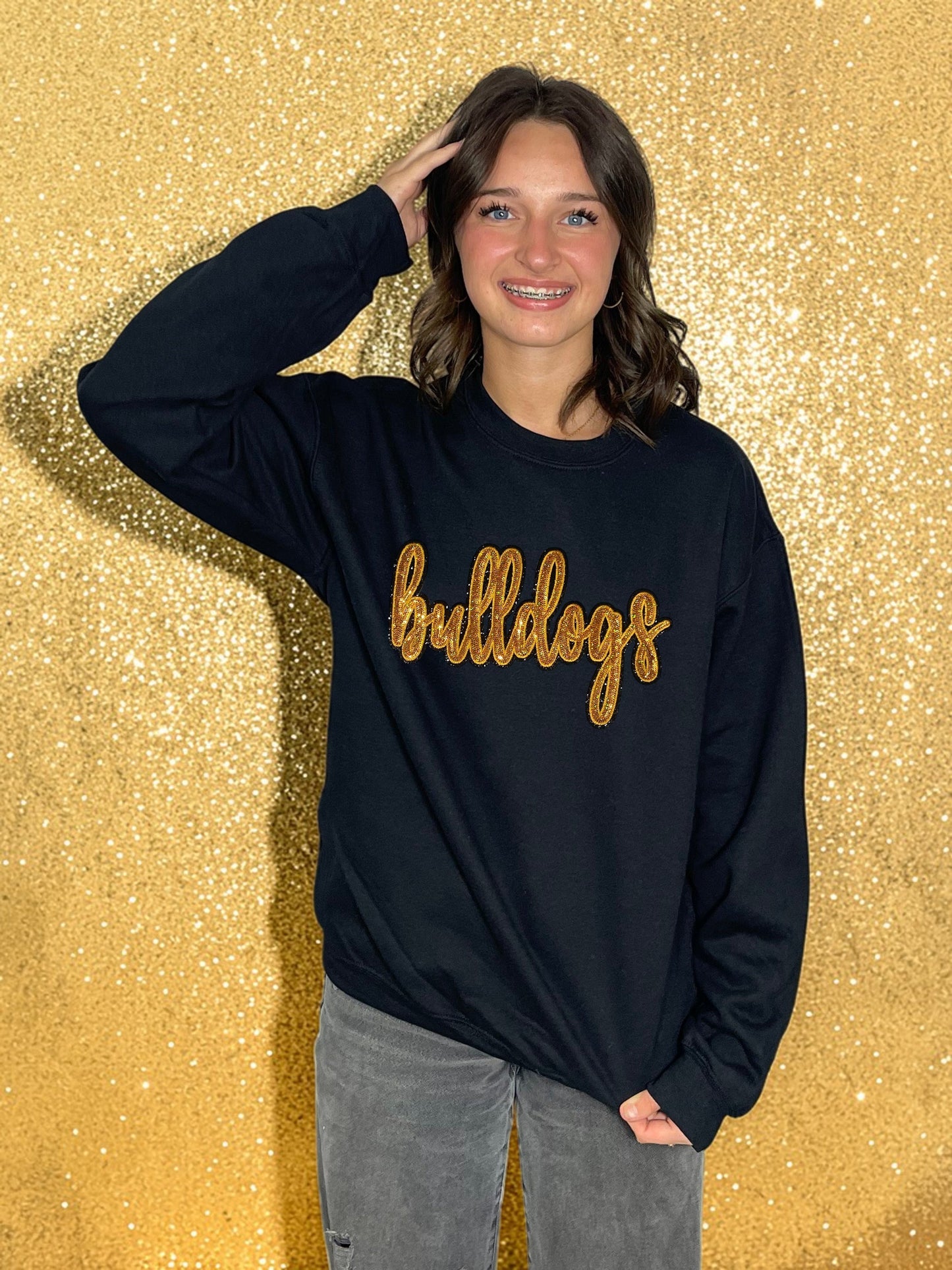Person wearing a black sweatshirt with 'bulldogs' in gold letters against a glittery gold background